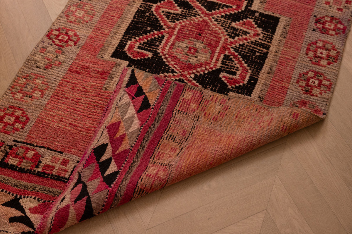 Handmade pink and black wool-cotton Persian-style runner rug with geometric bohemian patterns.