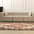 A modern sectional sofa in a light beige fabric, styled in a minimalist living room next to a large red and beige patterned oriental rug.
