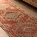 Handmade pink and brown Persian-style wool and cotton runner rug with geometric patterns on a wooden floor.