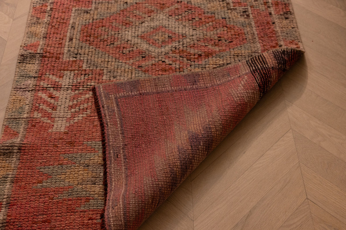Handmade pink and brown wool-cotton Persian-style runner rug with geometric patterns on a wooden floor.