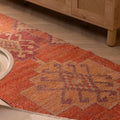 Handmade orange wool and cotton Persian-style runner rug with floral and geometric patterns on a wooden floor.