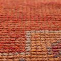 Close-up of a handmade wool and cotton Persian-style runner rug with orange floral patterns and a textured low-pile weave.