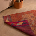 Handmade wool and cotton Persian-style runner rug in orange with floral patterns and a folded corner detail.