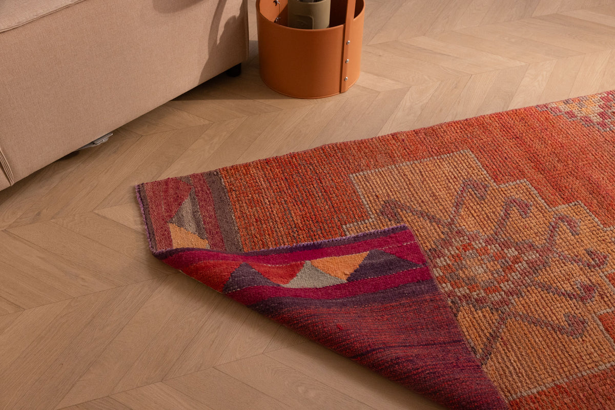 Handmade wool and cotton Persian-style runner rug in orange with floral patterns and a folded corner detail.