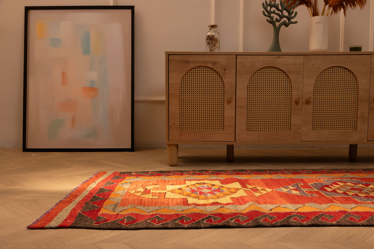 Handmade red and orange Persian-style wool and cotton Kilim runner rug with geometric patterns on a wooden floor.