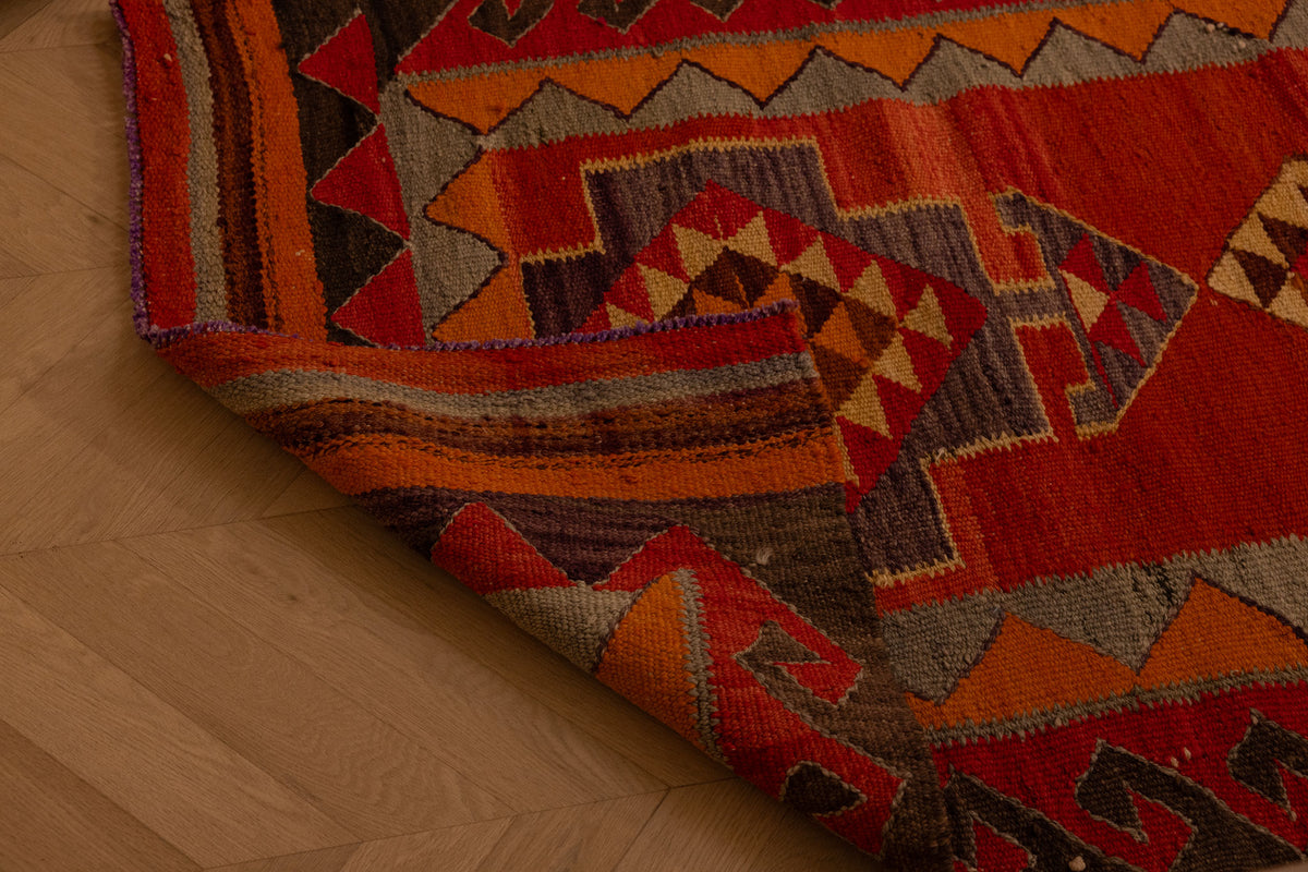 Handmade wool and cotton Persian-style Kilim runner rug in red and orange with geometric patterns on a wooden floor.
