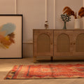 Handwoven pink and beige Persian-style wool and cotton runner rug with geometric patterns on a wooden floor.