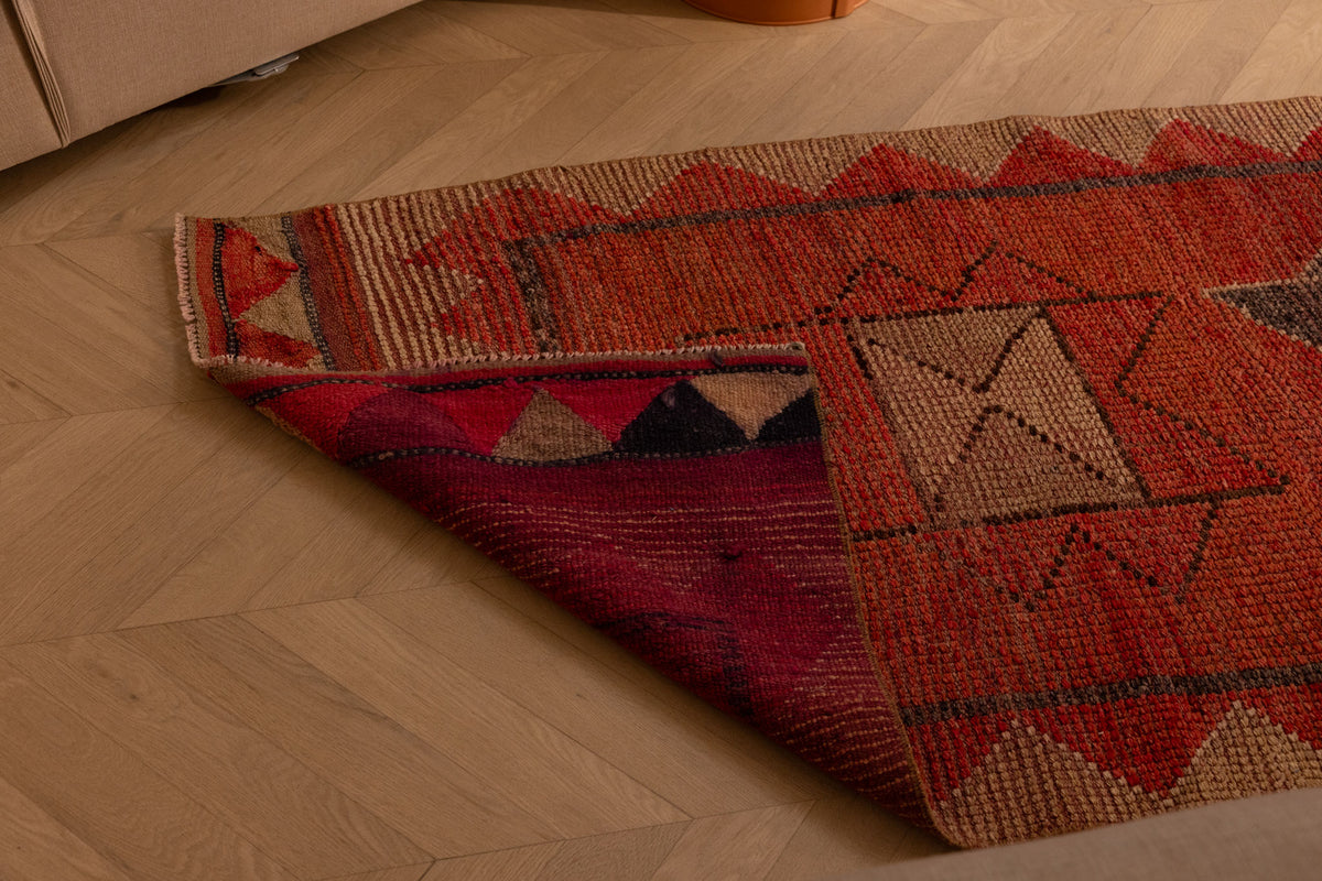 Handmade pink and beige wool-cotton Persian runner rug with geometric patterns on a wooden floor.