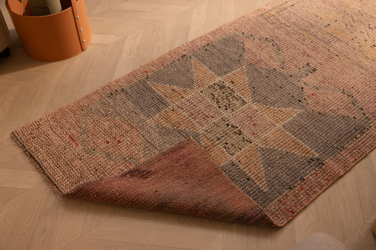 Handmade pink and brown wool-cotton Persian runner rug with geometric patterns on a wooden floor.