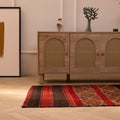 Handmade vintage Turkish wool kilim rug in red and brown with geometric patterns on a wooden floor.