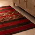 Handmade 3x5 ft vintage Turkish wool kilim rug in red and brown with geometric patterns on a wooden floor.