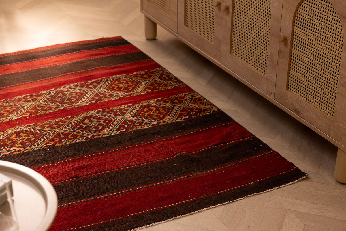 Handmade 3x5 ft vintage Turkish wool kilim rug in red and brown with geometric patterns on a wooden floor.