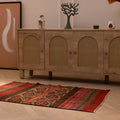 Hand-woven 3x4 ft vintage Turkish wool rug in red and brown with geometric patterns on a light wood floor.