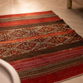 Handmade 3x4 ft vintage Turkish wool kilim rug with red and brown geometric patterns on a light wood floor.