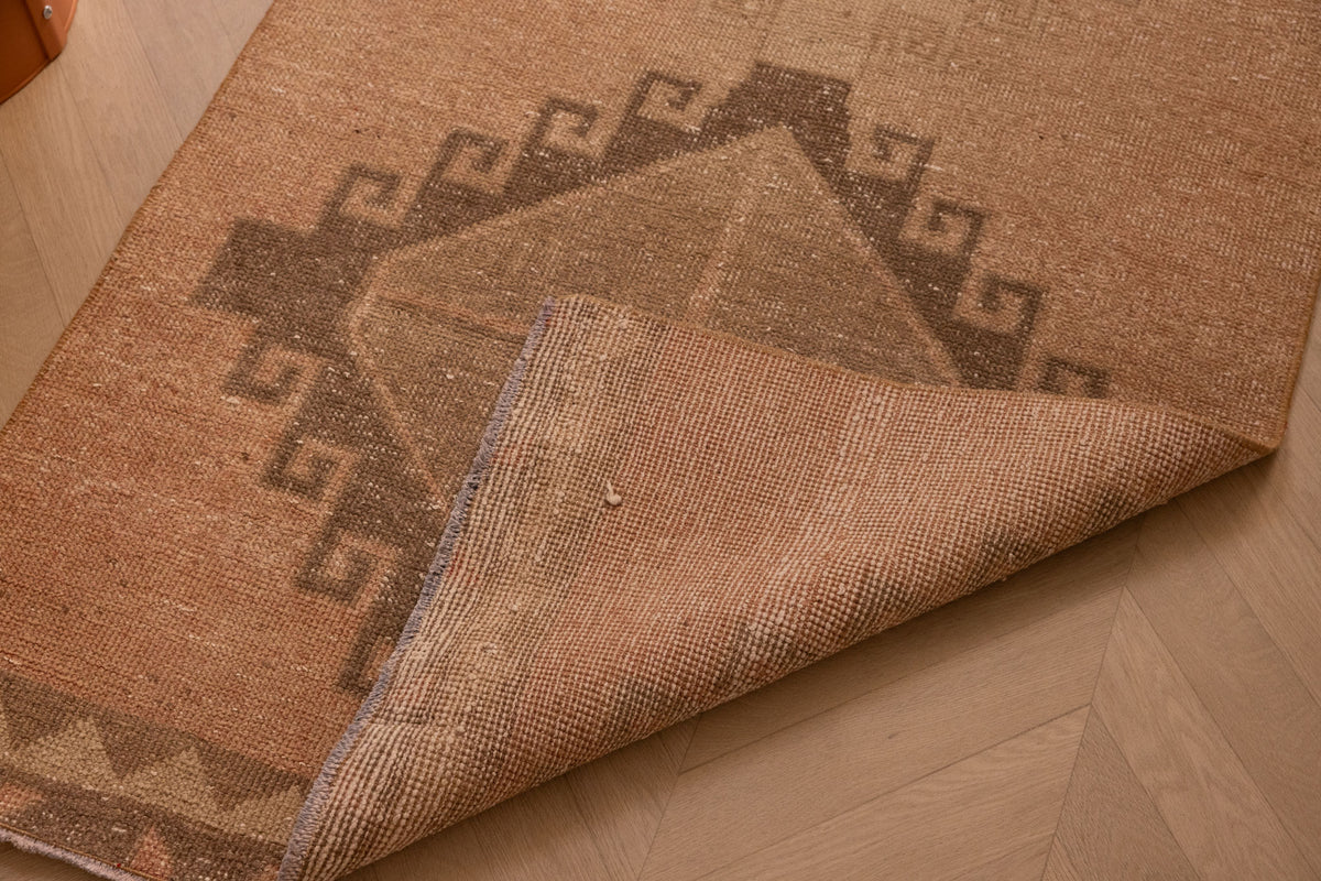 Vintage 3x12 ft Turkish runner rug in orange and brown wool with geometric tribal patterns and a folded corner.