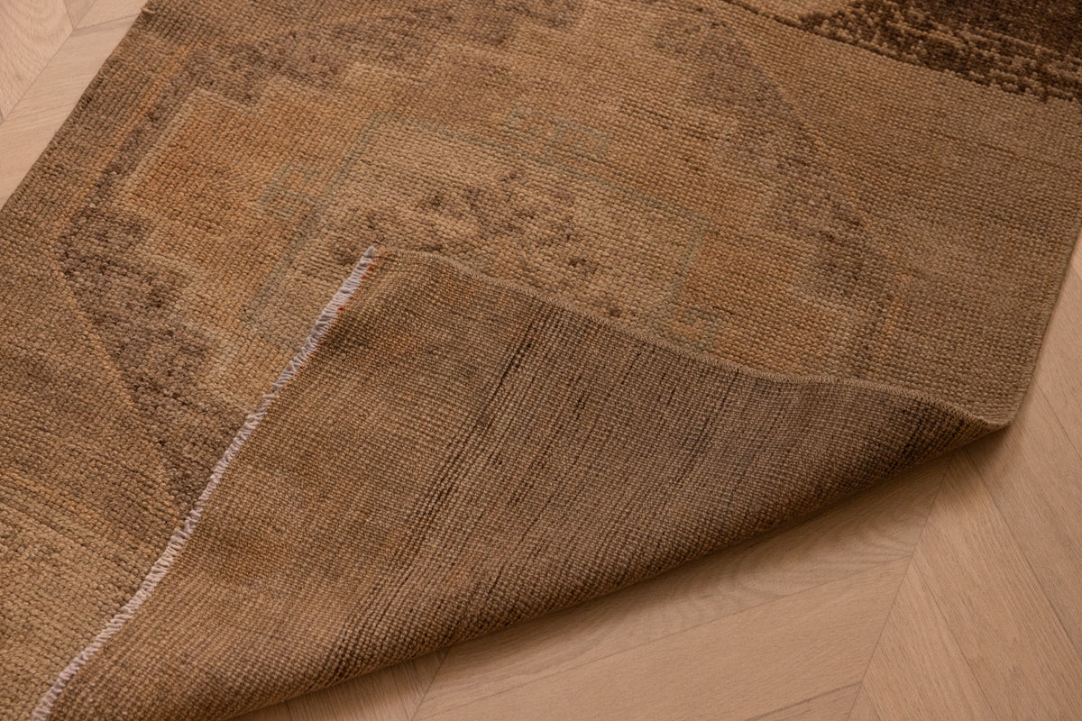 Hand-woven vintage Turkish runner rug in beige and brown wool with geometric patterns and a folded corner.