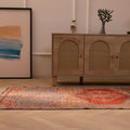 Handmade wool and cotton Persian style runner rug in orange and brown with geometric patterns on a wooden floor.