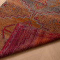 Handmade wool and cotton Persian-style runner rug in orange and brown with geometric patterns on a wooden floor.