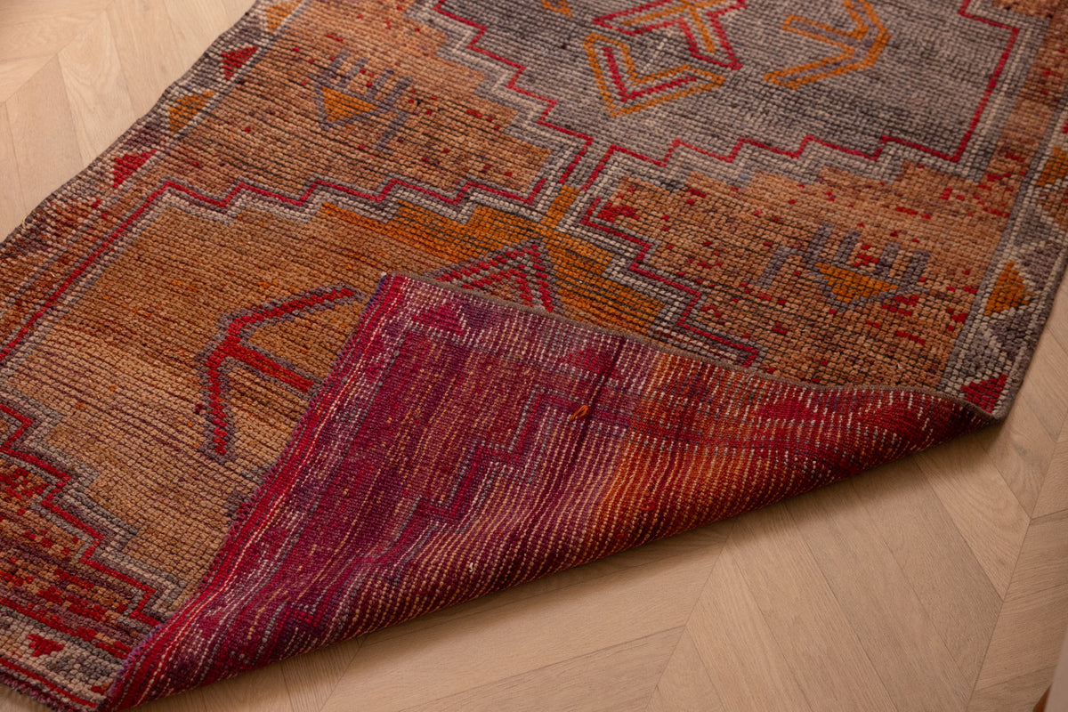 Handmade wool and cotton Persian-style runner rug in orange and brown with geometric patterns on a wooden floor.