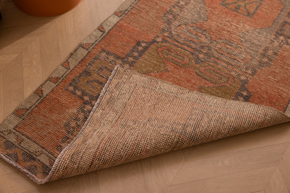 Handwoven vintage Turkish runner rug in brown and orange with geometric patterns, showing wool and cotton weave texture.