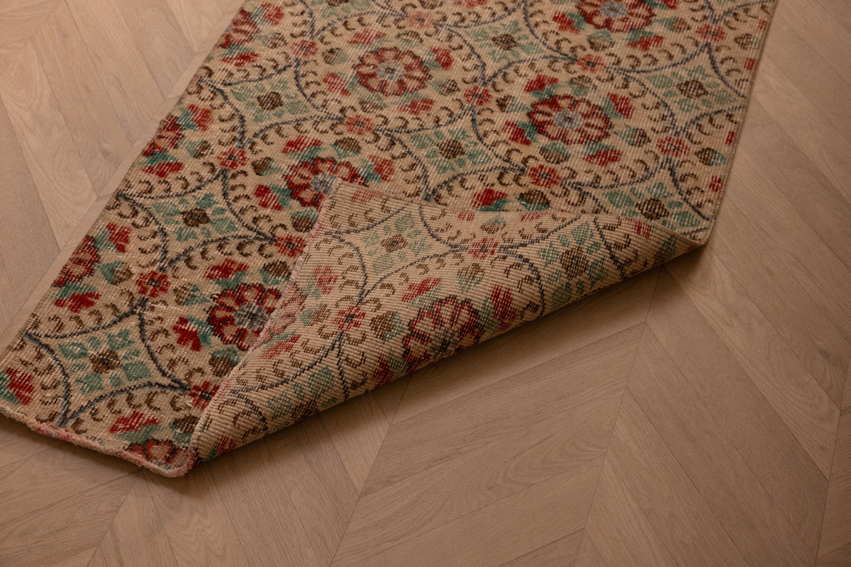 Vintage 2x8 ft handmade Turkish runner rug in beige and green with floral patterns on a herringbone wood floor.