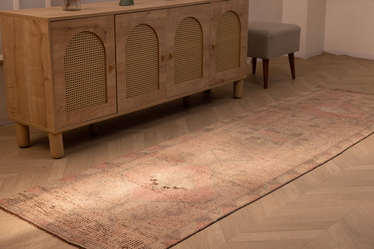 Handmade pink and beige Persian style wool-cotton runner rug with geometric patterns on a herringbone wood floor.