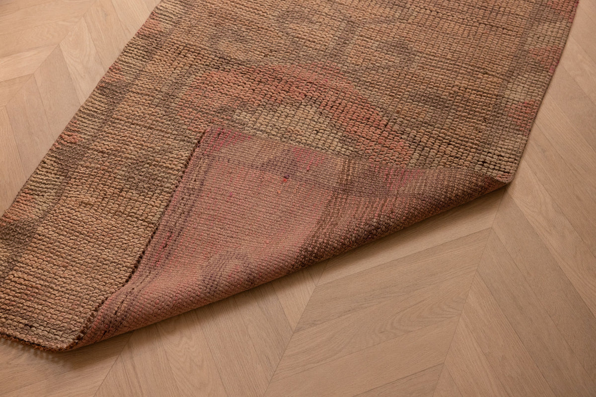 Handmade pink and beige wool-cotton Persian style runner rug with geometric patterns on herringbone wood flooring.