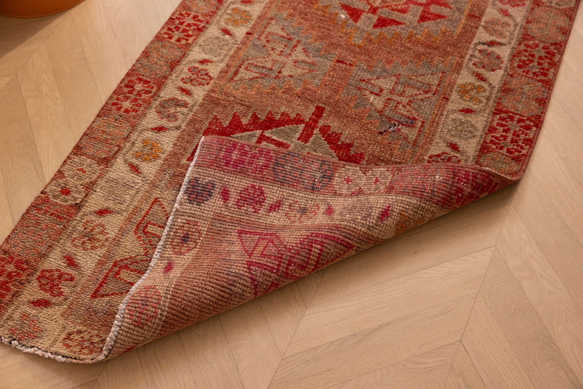 Handmade brown and red Persian-style wool-cotton runner rug with floral and geometric patterns on a wooden floor.