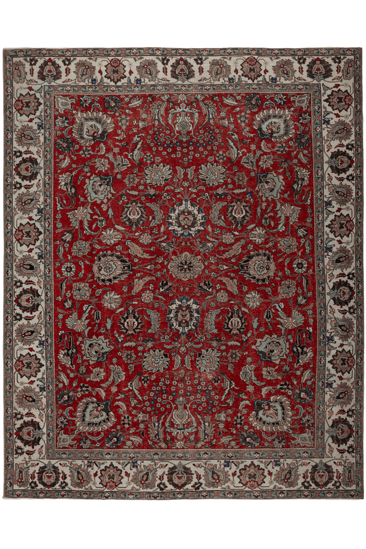 A traditional oriental-style area rug with a deep red field, featuring an intricate floral and medallion pattern in beige, gray, and black, surrounded by a detailed multi-colored border.