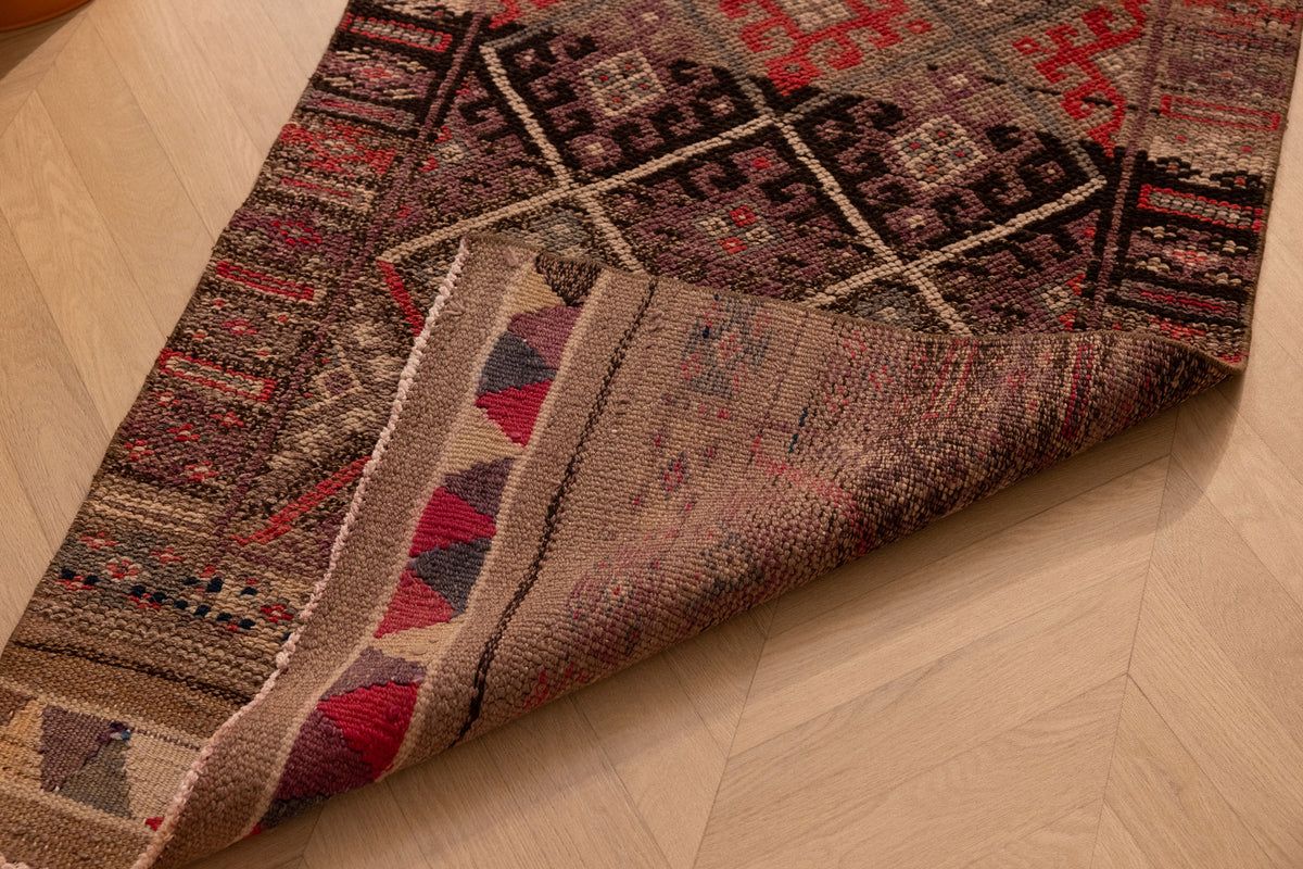 Handmade brown wool and cotton Persian-style runner rug with geometric maximalist patterns on a wooden floor.
