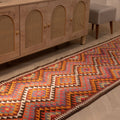 Handmade 3x11 ft Persian-style wool and cotton kilim runner with pink and orange geometric patterns on a wooden floor.