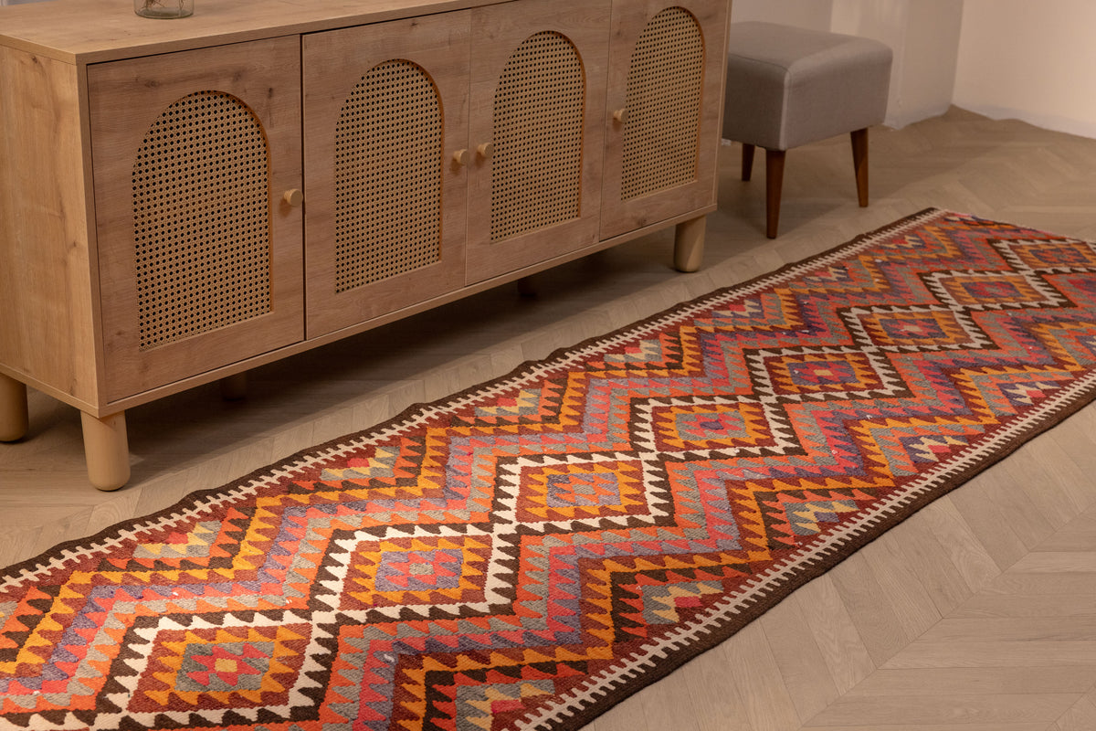 Handmade 3x11 ft Persian-style wool and cotton kilim runner with pink and orange geometric patterns on a wooden floor.