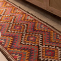 Handmade 3x11 ft wool and cotton Persian-style kilim runner featuring pink and orange geometric patterns.