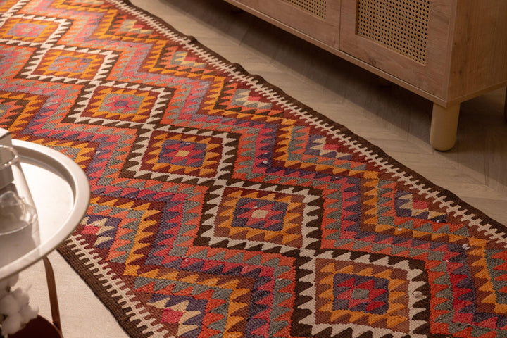 Handmade 3x11 ft wool and cotton Persian-style kilim runner featuring pink and orange geometric patterns.