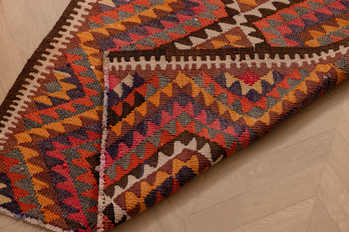 Handmade pink and orange Persian-style wool-cotton kilim runner with geometric patterns on a wooden floor.