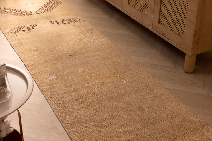 Hand-woven 2x11 ft vintage Turkish runner rug in beige and brown with geometric patterns on a wooden floor.