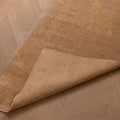 Hand-woven beige and brown vintage Turkish runner rug with a folded corner on a herringbone wood floor.