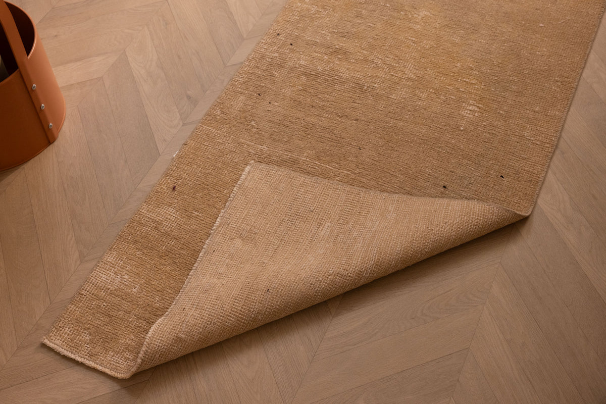 Hand-woven beige and brown vintage Turkish runner rug with a folded corner on a herringbone wood floor.