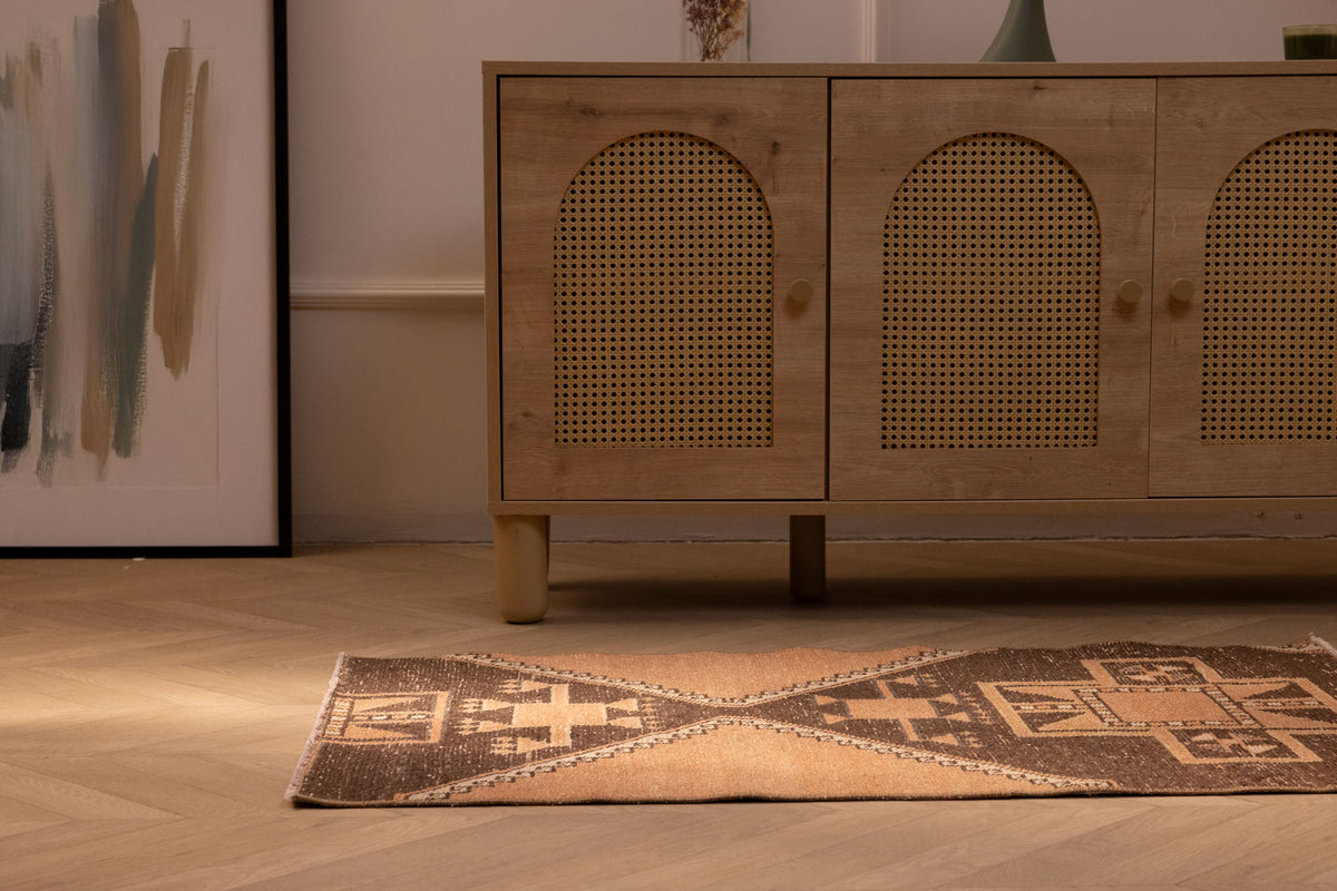 Hand-woven 2x4 ft vintage Turkish wool rug with orange and brown geometric patterns on a wooden floor.