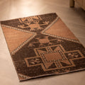 Hand-woven 2x4 ft vintage Turkish wool doormat featuring orange and brown geometric patterns on a wooden floor.