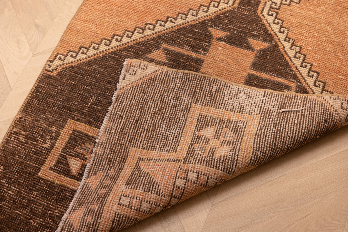 Hand-woven 2x4 ft vintage Turkish doormat in orange and brown wool-cotton with geometric patterns.