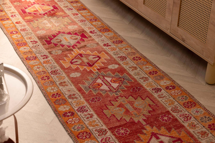 Handmade 13.5ft wool and cotton runner rug in red and orange with a bohemian floral pattern.