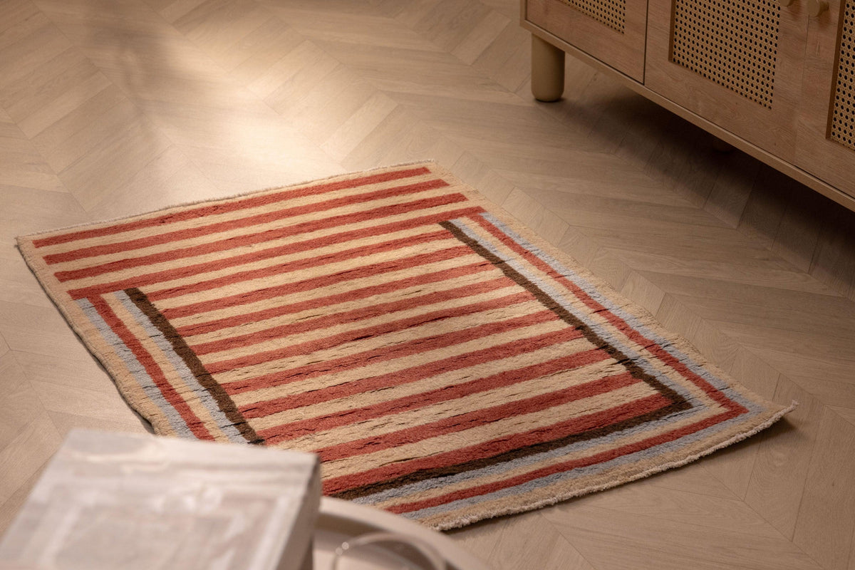 Handmade 2x3 ft vintage Turkish Isparta rug with red and beige stripes on a wooden herringbone floor.