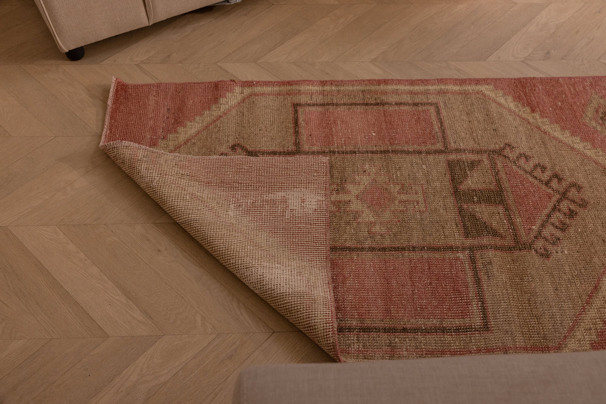 Hand-woven vintage Turkish runner rug in pink and gray geometric patterns, made of wool and cotton on a wooden floor.