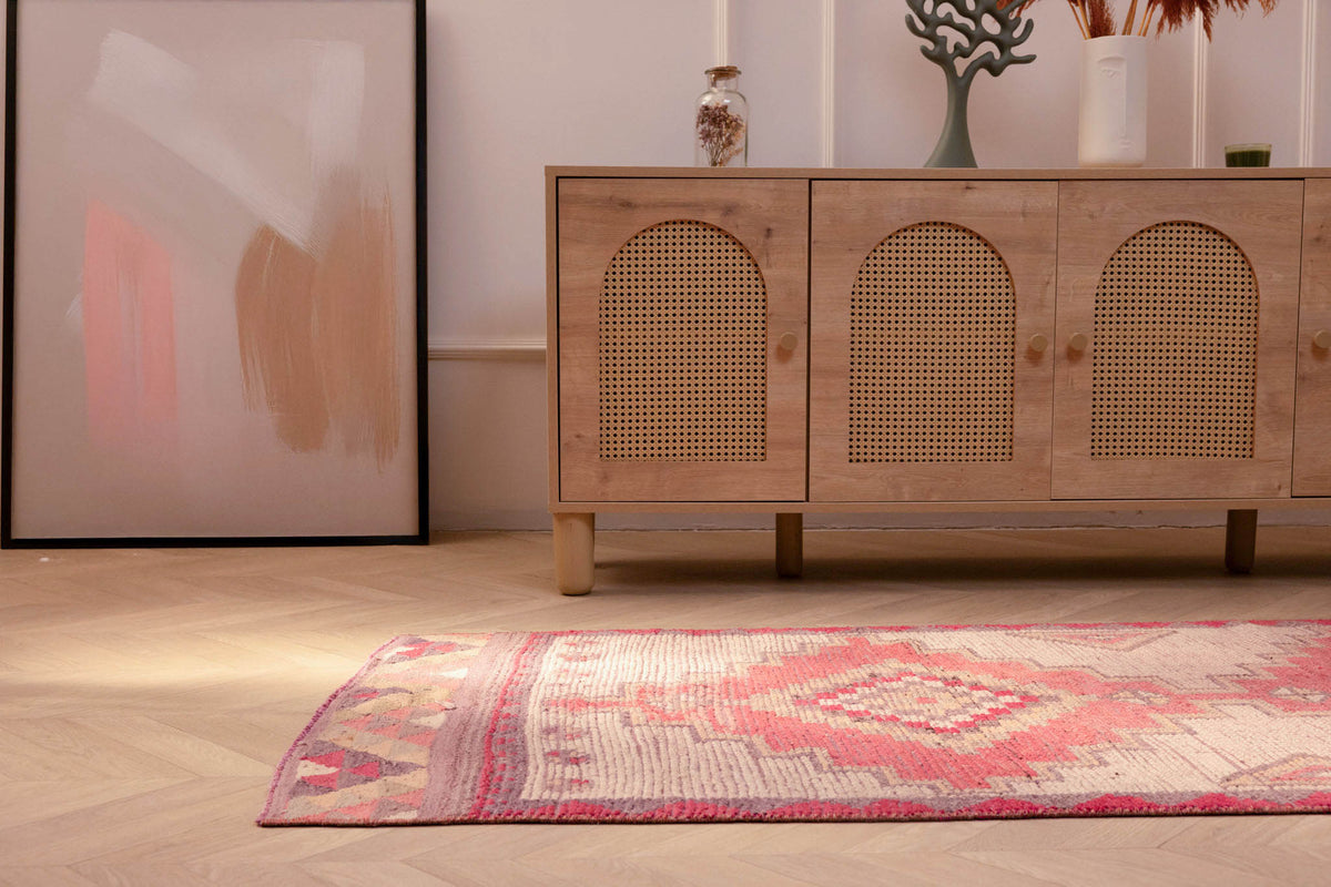 Handmade pink and white Persian-style wool-cotton runner rug with geometric patterns on a herringbone floor.