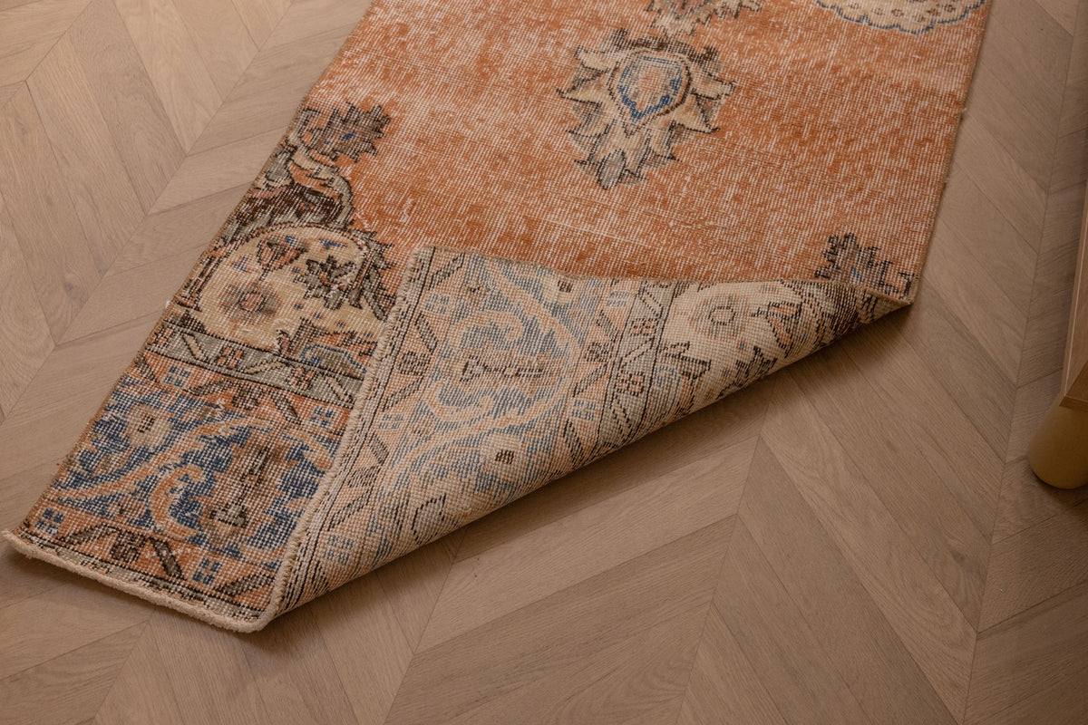 Vintage Isparta wool and cotton runner rug in burnt orange with blue floral patterns on a herringbone wood floor.