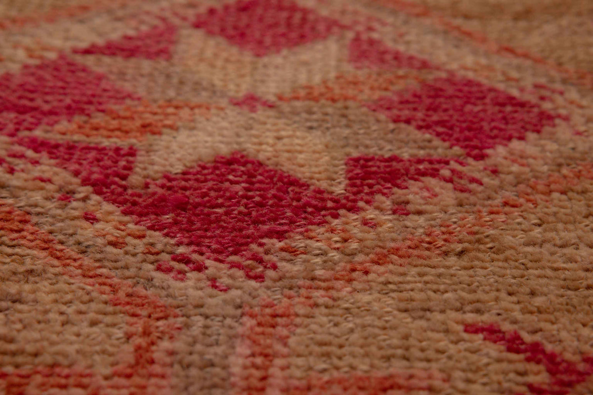 Close-up of a handmade wool and cotton runner rug featuring a brown and pink floral, maximalist Persian-style pattern.