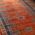 Handmade vintage Persian-style runner rug in orange and navy with a rustic floral pattern, crafted from wool and cotton.