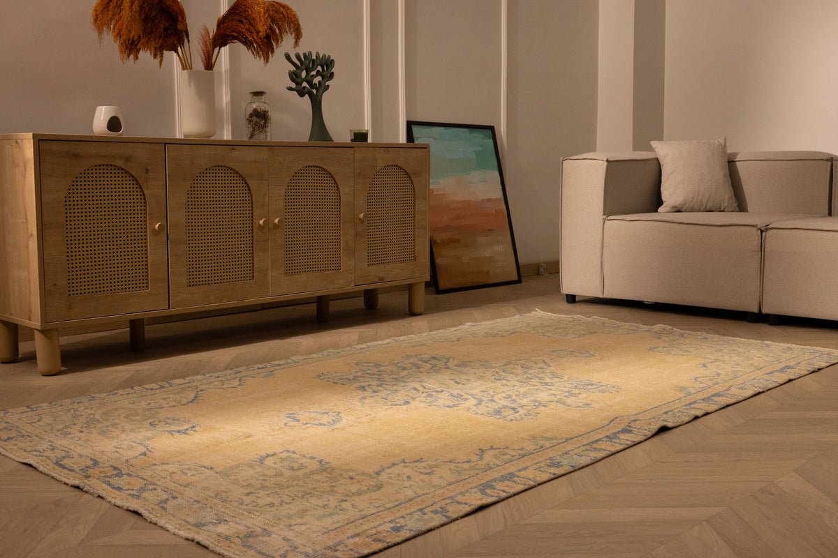 Hand-woven 4x8 ft vintage Turkish rug in yellow and blue with traditional floral patterns on a wooden floor.