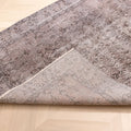 Vintage gray overdyed Isparta Turkish wool and cotton rug with floral patterns and a folded corner on a wooden floor.